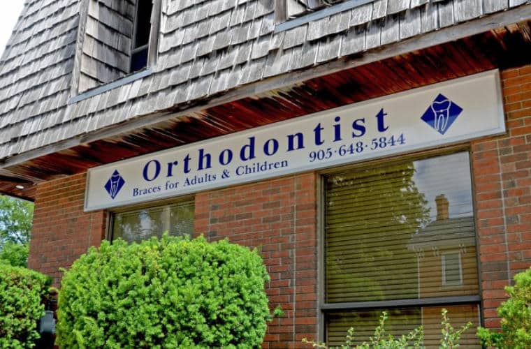 A red brick building with a sign for Ancaster Orthodontics above two windows.