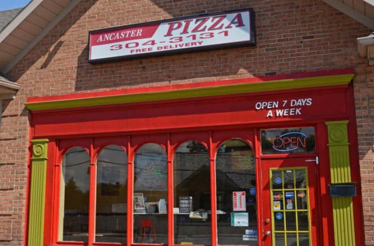 The front entrance of Ancaster Pizza with a sign above it.