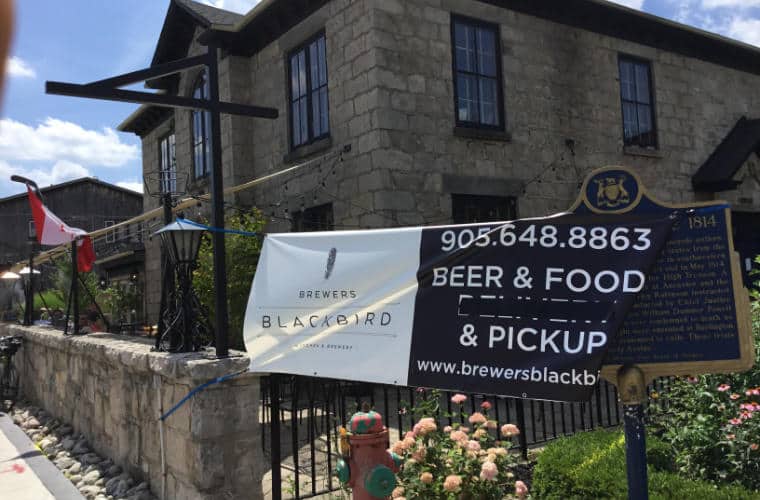A square grey stone building with black framed windows and a sign for Brewers Blackbird Kitchen out front.