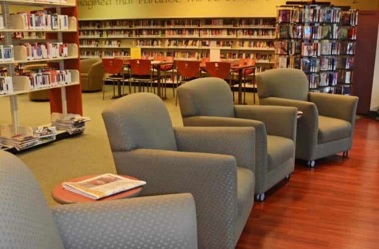 A large room lined with bookshelves and four arm chairs in the foreground.