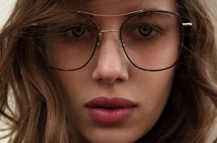 A close up of a woman's face with wavy brown hair and wearing large thin rimmed glasses.