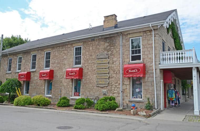 A rough hewn beige stone building with signs for Kari's of Ancaster on awnings above the windows.