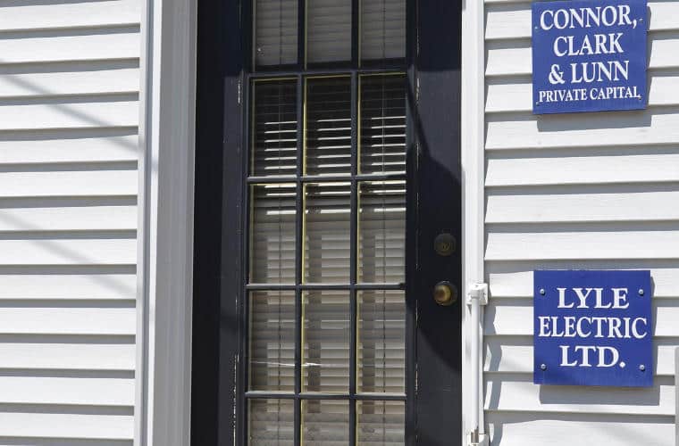 A black door on the front of a white sided building with a sign for Lyle Electric beside it.