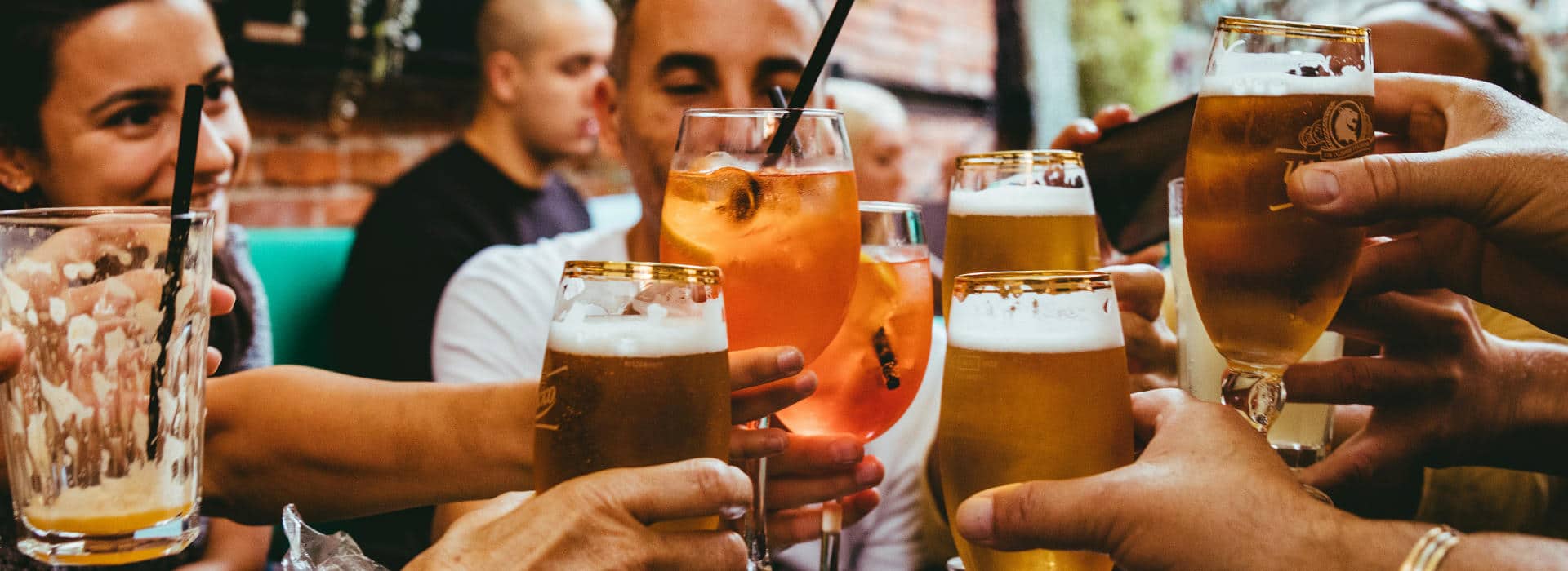 A group of people on a patio cheersing pints of beer.