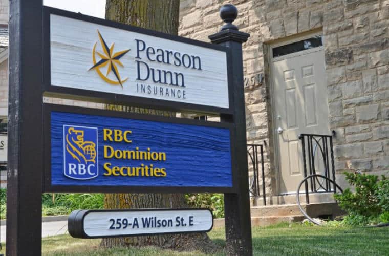 The entrance of a rough hewn beige stone building with a sign for RBC Wealth Management on the front lawn.