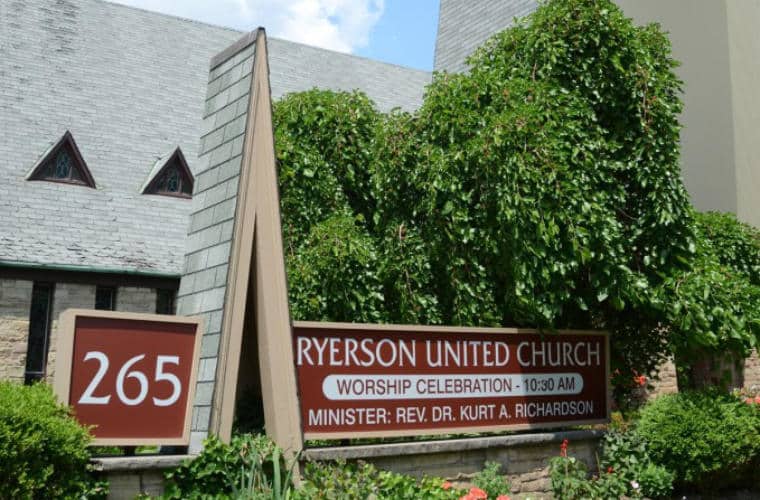 A sign for Ryerson United Church surrounded by green bushes.