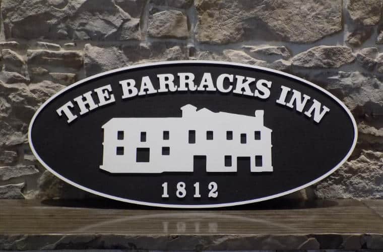 A sign for The Barracks Inn on a rough hewn grey brick wall.