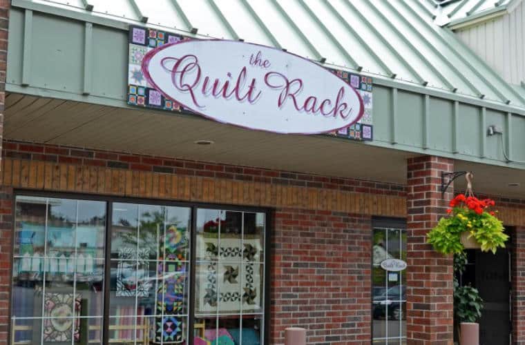 A red brick building with a large front window and a sign for The Quilt Rack above it.