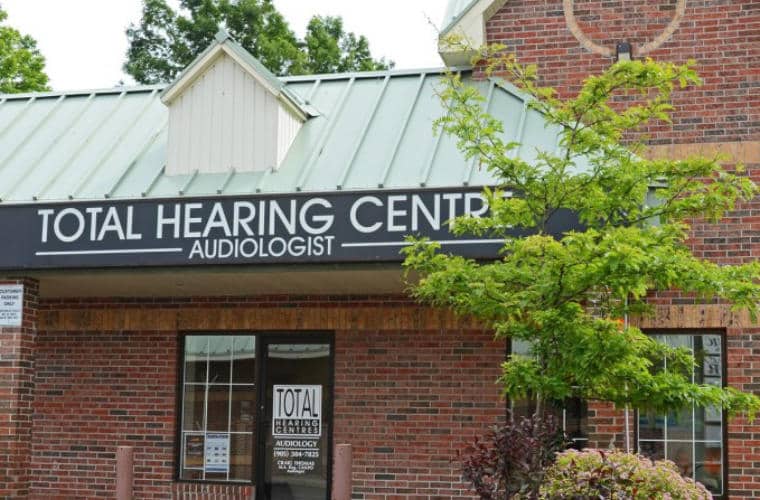 A red brick building with green roofing and a sign for Total Hearing Centre above the entrance.